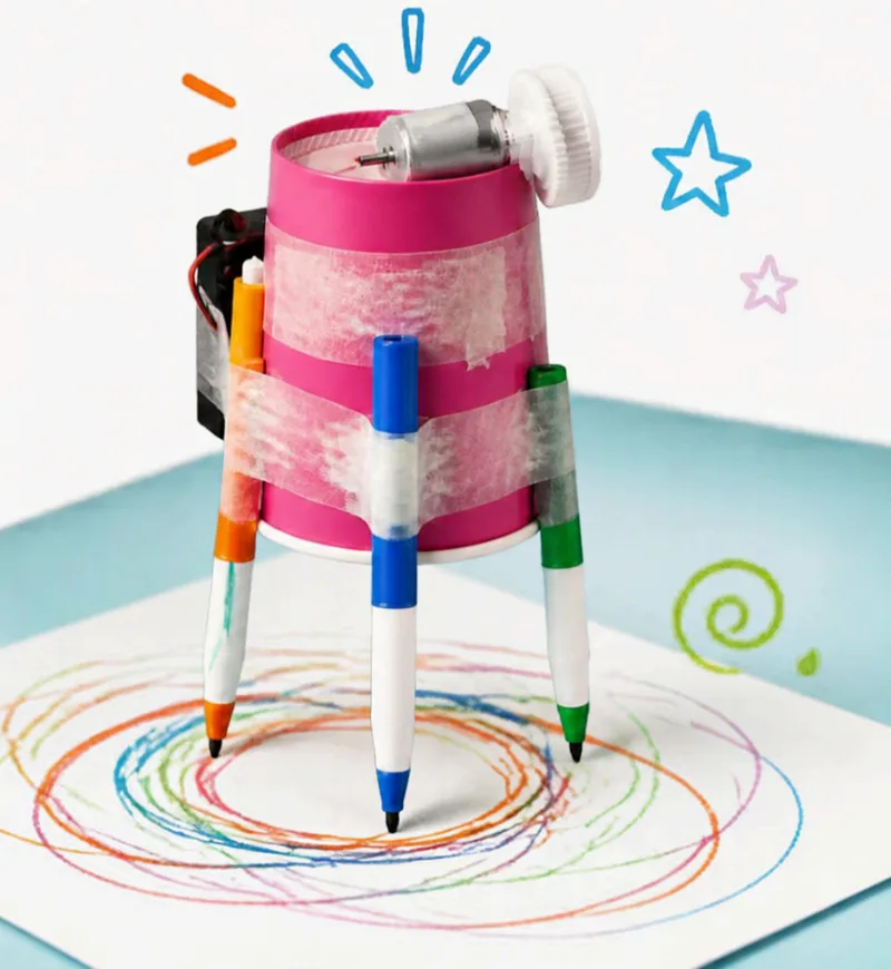 Robot fatto con un bicchiere rosa e tre pennarelli come gambe, che disegna cerchi colorati su un foglio